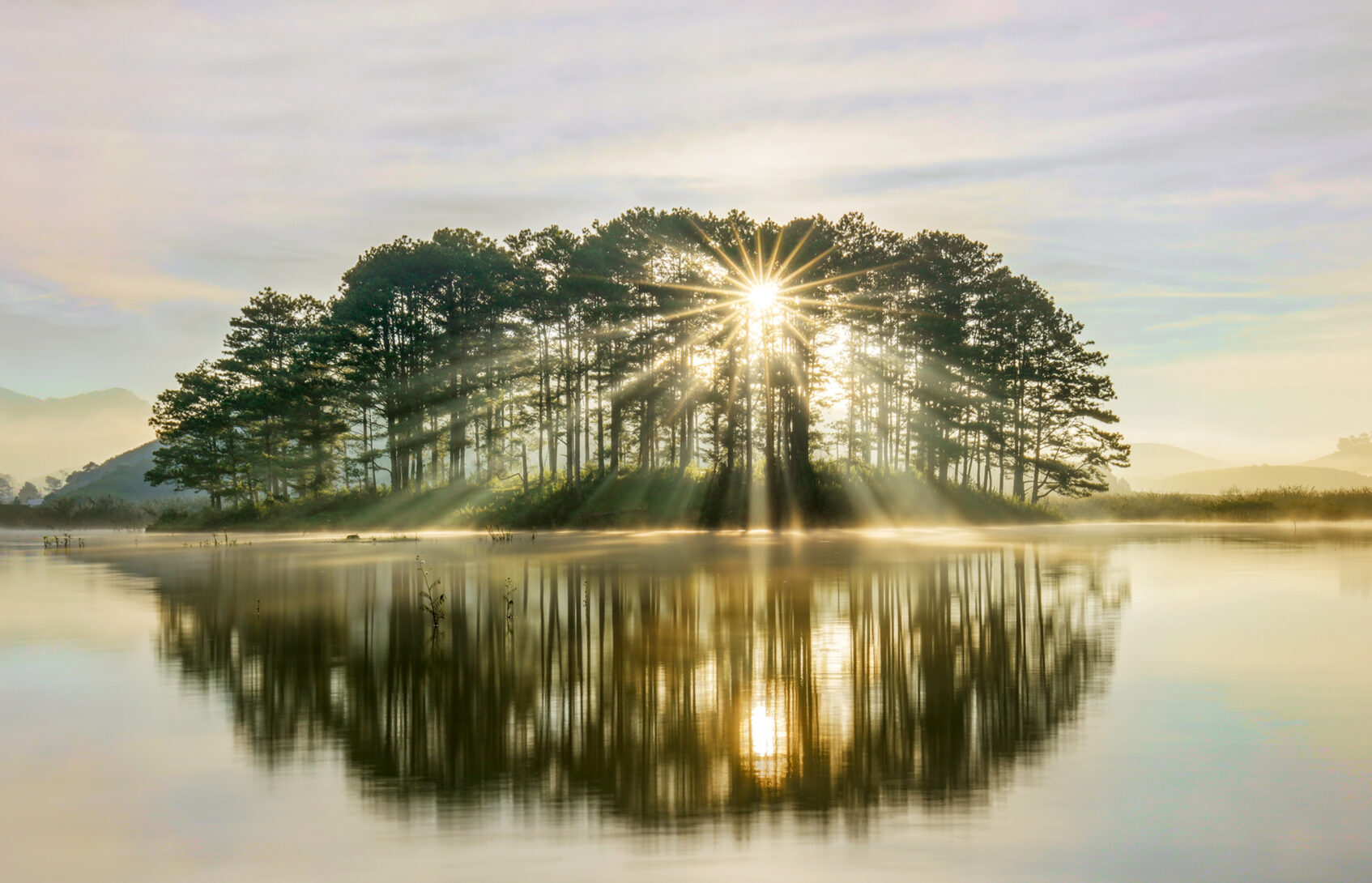 The sun shines through trees on an island surrounded by water.