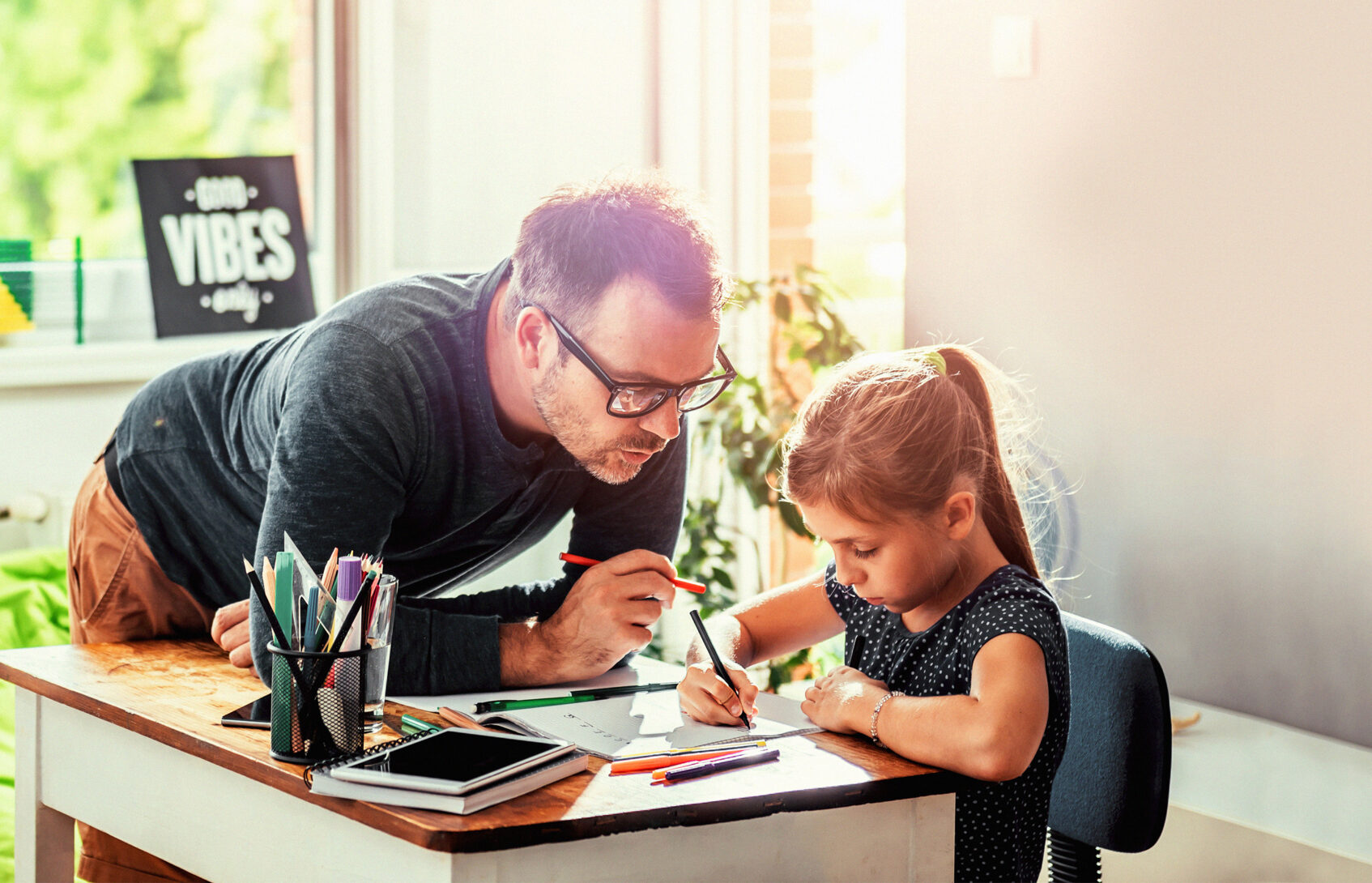 A dad and his young daughter writing in a notebook.