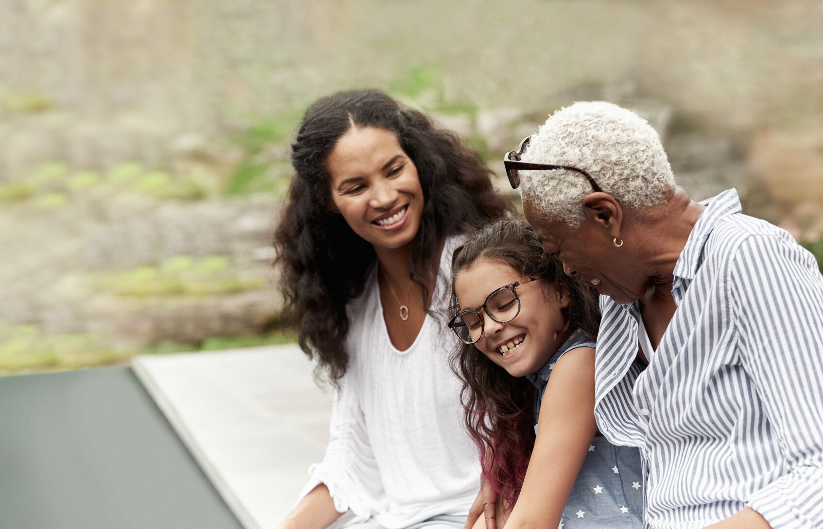 Grandmother, daughter, granddaughter seated by backyard pool