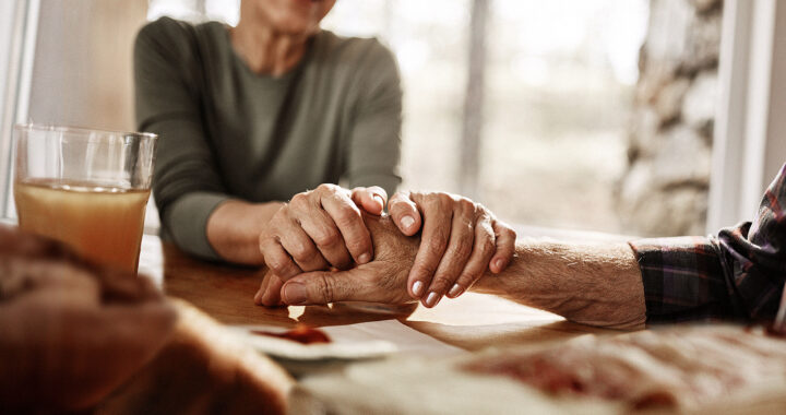 Woman seated at a table holding a man’s hand.