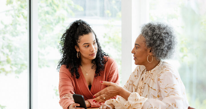 Two women seated at a table talking and holding a mobile phone