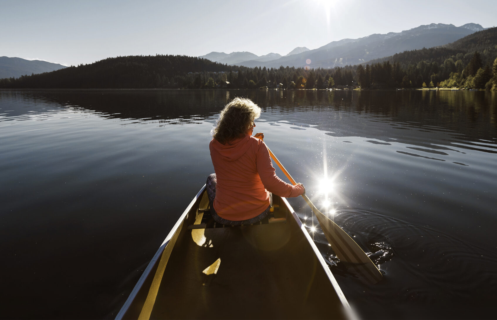 Woman paddling a canoe on a lake.