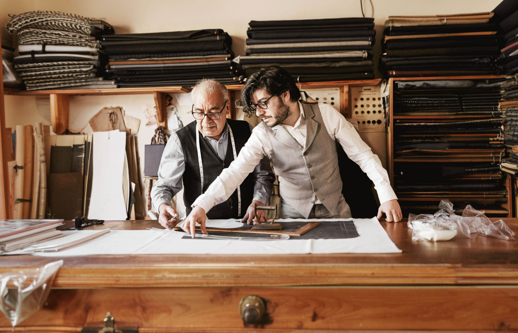 A father and son measuring fabric together in a tailor shop.