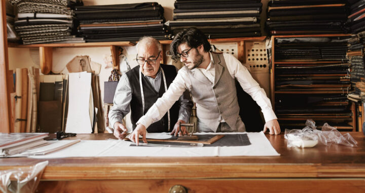 A father and son measuring fabric together in a tailor shop.
